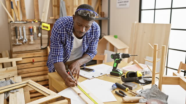 Handsome black man measuring wood in a sunny carpentry workshop, conveying craftsmanship and skill.