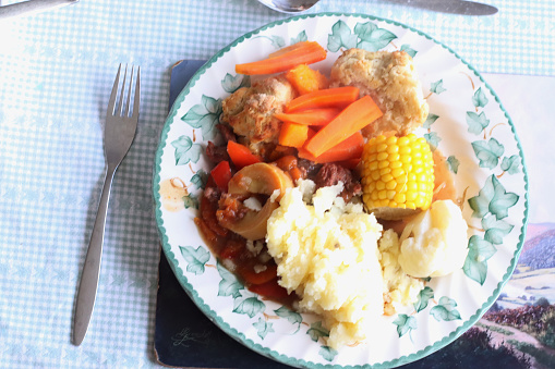 Elderly's hand preparing Sunday Lunch traditional UK British English food with dumpling carrot mash potato sweet corn cob and gravy sauce. Top view copy space.