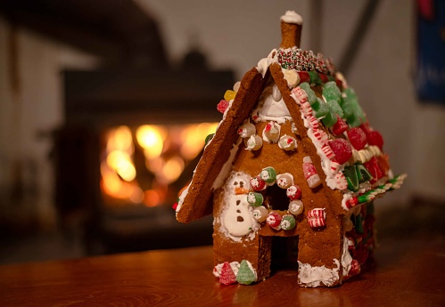 Bokeh firepace background with copy space and no people. Homemade child's gingerbread house in foreground with candy and icing warm welcoming holiday scene