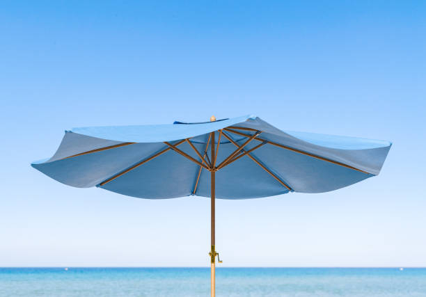 3D rendering of a close-up view of a blue beach umbrella with its structure contrasted against a clear sky and tranquil ocean backdrop. Summer vacation concept
