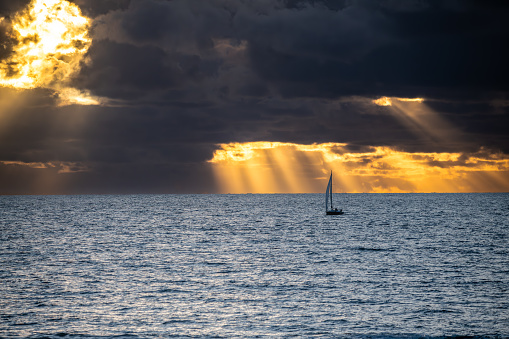 a boat taking hte sea while the sunset pierce through the sky