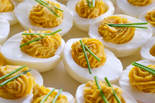 Closeup of stuffed eggs with two sprigs of chives on a white plate on a wooden table. Image with copy space.