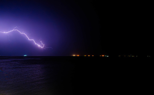 A flash of purple lightening amidst a small thunder storm on the coast of Greece.
