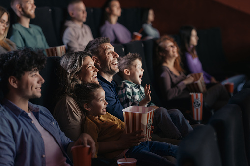 Cheerful parents and their kids having fun while watching a movie in cinema. Focus is on mother and daughter.