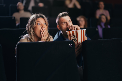 Shocked couple watching a crime movie in theatre. Focus is on woman.