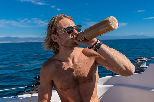 Blonde man drinking from a bottle on a sailing boat by the Mediterranean Sea in south Spain