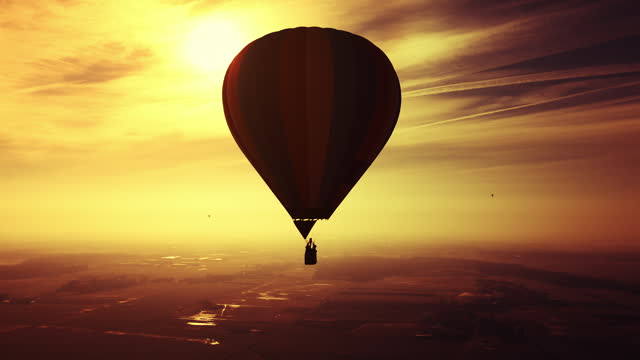 AERIAL Drone Shot of Hot Air Balloon Flying Under Orange Sky in Countryside During Golden Hour