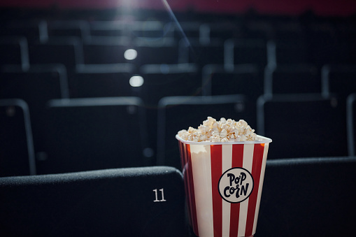 A cheerful multiethnic young adult couple are in a movie theater having fun while watching a movie, enjoying popcorn and soda.