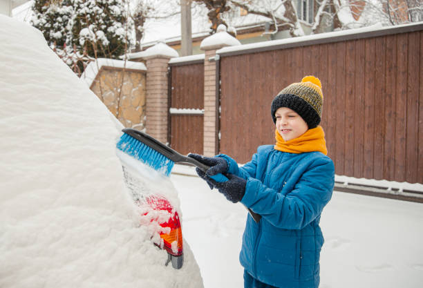 il ragazzino carino sta aiutando suo padre a spazzolare la neve dall'auto. rimozione della neve dal concetto di auto di cura dell'auto durante - snow car window ice scraper foto e immagini stock