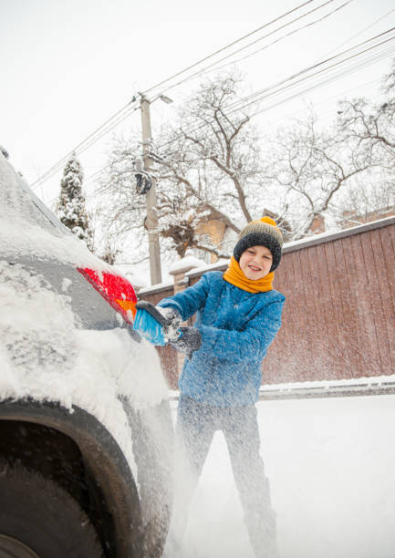 il ragazzino carino sta aiutando suo padre a spazzolare la neve dall'auto. rimozione della neve dal concetto di auto di cura dell'auto durante - snow car window ice scraper foto e immagini stock