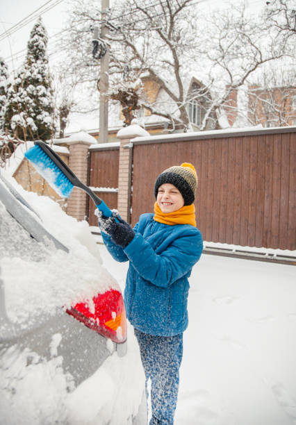 il ragazzino carino sta aiutando suo padre a spazzolare la neve dall'auto. rimozione della neve dal concetto di auto di cura dell'auto durante - snow car window ice scraper foto e immagini stock