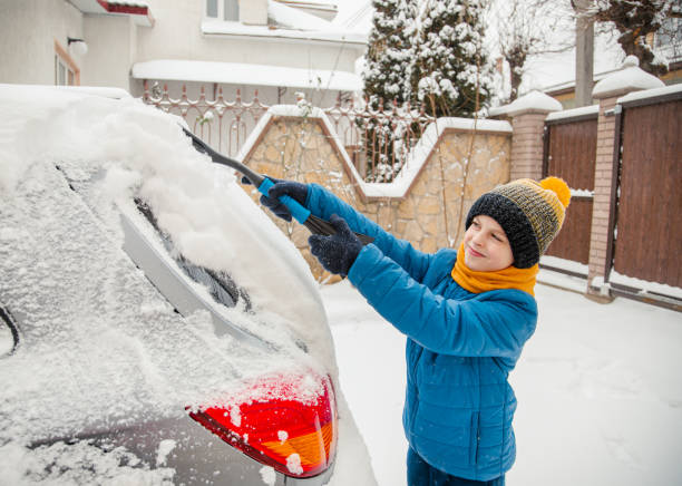 cute little boy is helping his father brush the snow from the car. snow removal from the car concept of car care during - snow car window ice scraper foto e immagini stock