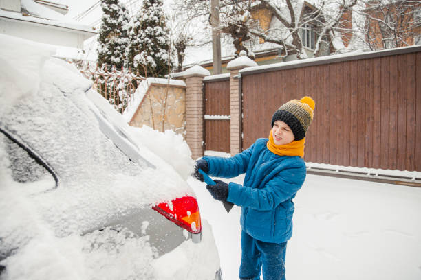 il ragazzino carino sta aiutando suo padre a spazzolare la neve dall'auto. rimozione della neve dal concetto di auto di cura dell'auto durante - snow car window ice scraper foto e immagini stock