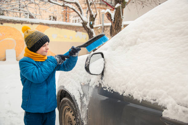 il ragazzino carino sta aiutando suo padre a spazzolare la neve dall'auto. rimozione della neve dal concetto di auto di cura dell'auto durante - snow car window ice scraper foto e immagini stock