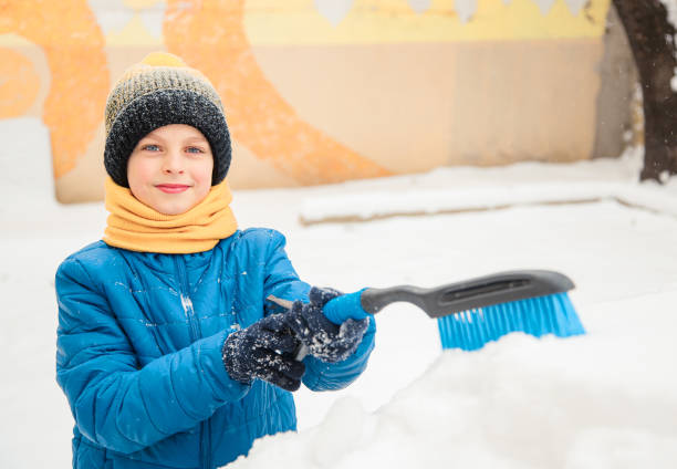 il ragazzino carino sta aiutando suo padre a spazzolare la neve dall'auto. rimozione della neve dal concetto di auto di cura dell'auto durante - snow car window ice scraper foto e immagini stock