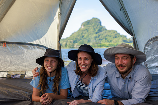 Portrait of happy Caucasian family lying inside tent on vacations, by the lake, at campground