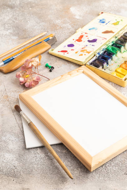 istock Drawing accessories set: brushes, pencils, watercolor, frame on brown concrete. Side view 1937018672