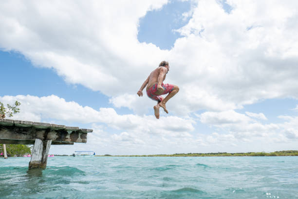 istock Happy young man jumping from pier into beautiful lake 1937019197