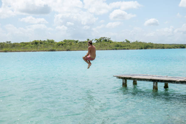istock Happy young man jumping from pier into beautiful lake 1937019198