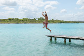Happy young man jumping from pier into beautiful lake
