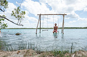 Young man relaxing on swing in a beautiful lagoon on a sunny day