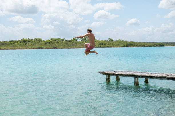 istock Happy young man jumping from pier into beautiful lake 1937024125