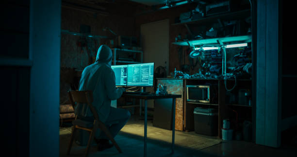 home garage late at night: evil male hacker wearing hoodie breaks into data servers, ddos attack, phishing attack, malware. man writing code for trojan horse virus. darknet cyber crime concept. - hacker - fotografias e filmes do acervo