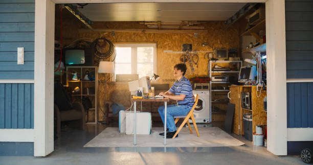 istock Caucasian Male Software Engineer Entering Retro Garage And Sitting At His Work Desk With Old Desktop Computer. Focused Man Starting Software Startup Company In Nineties, Working On Digital Product. 1937028452