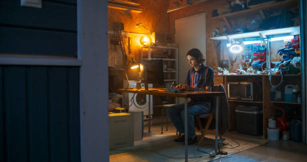 istock Wide Shot Of Caucasian Male Software Engineer Coding on Old Desktop Computer In Retro Garage In The Evening. Man Starting Tech Startup Company In Nineties. Coding Innovative Online Service At Home. 1937028471