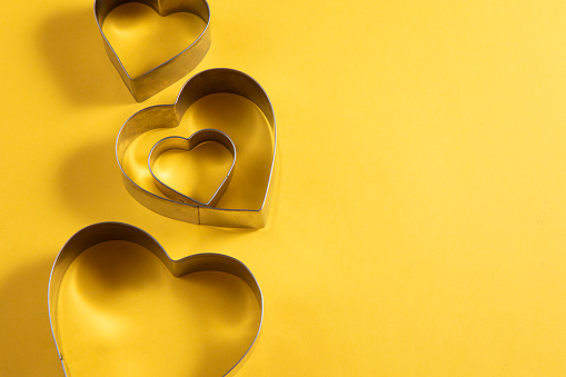 Heart shaped cookie cutters on yellow background with copy space