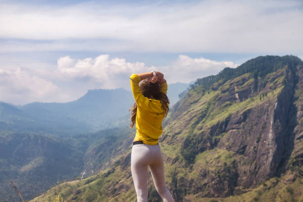 Rear view of adult woman enjoying at landscape Adam's peak mountain in tropical journey Sri Lanka, Ella. From behind of lady in yellow jacket posing at landmark nature background. Copy ad text space vista trasera de la mujer adulta que disfruta en el paisaje de la montaña del pico de adán en el viaje tropical sri lanka, ella. desde detrás de la dama con chaqueta amarilla posando en el fondo de la naturaleza de referencia. copiar espacio de texto de