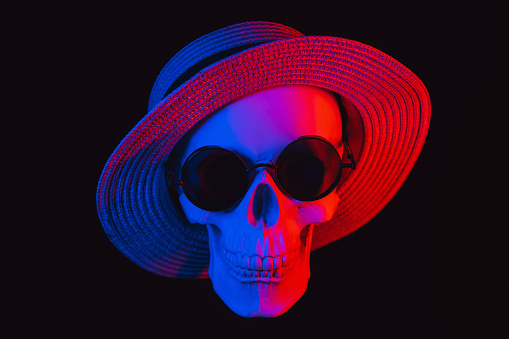 human skull wearing sunglasses and a hat with colored neon light on a dark background