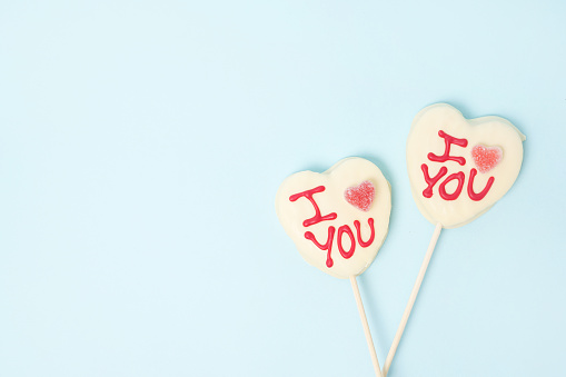 two Valentine's day heart shape candies with white chocolate on pastel blue paper background. Love Concept