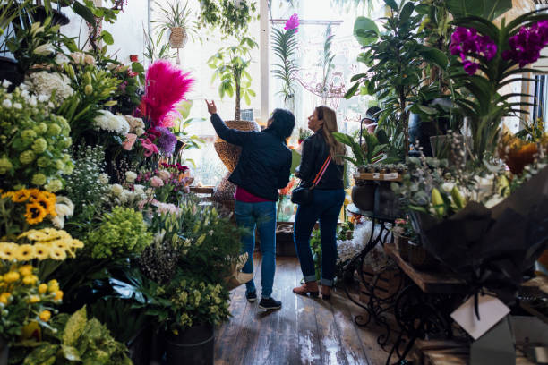 Two mature women shopping at a florist in Newcastle upon Tyne, England during a friends reunion city break. They are looking at and choosing from the beautiful flowers while having a discussion and pointing to the merchandise.