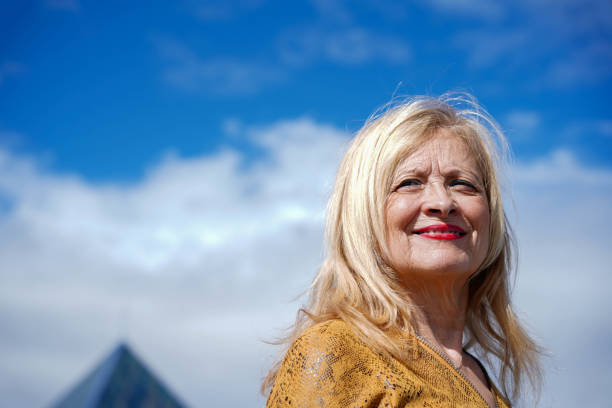 femme à la retraite souriante aux cheveux blonds avec ciel bleu en arrière-plan - clothing excitement mode of transport blond hair photos et images de collection