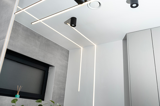 LED light strips mounted in the wall and ceiling in a modern bathroom, visible ventilation anemostat.