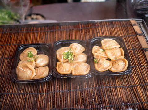 Stock photo showing an evening meal of pan fried dumplings (Momos), filled with mixed vegetables and pork drizzled with chilli oil and garnished with chopped chives and nigella seeds.