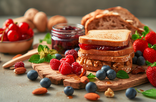 Sandwiches with peanut butter, jam, and fresh fruits on a white wooden background from the top view