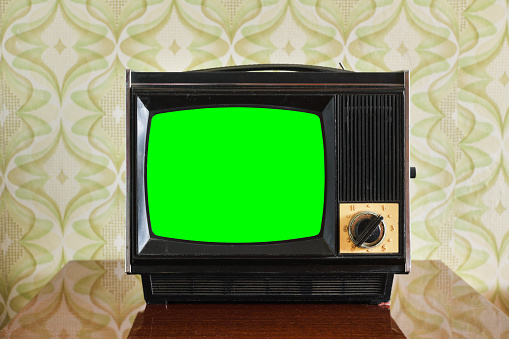 An old TV with a green screen on the nightstand against the background of wallpaper.