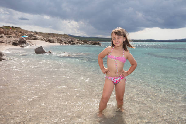 The wondrous and colorful waters of the Mediterranean sea on a summer day, on Monti Russu beach near Santa Teresa Gallura. A little girl is having a swim.