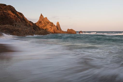 At dawn the first sun lights up the highest rock on Rena Majori beach, near Santa Teresa Gallura. Long waves throw their foam onto the sandy beach, still in darkness.