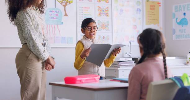 istock School book, child and reading in class for learning, development and communication. A smart girl kid or student and woman teacher for language story, support and confidence in elementary classroom 1937157453