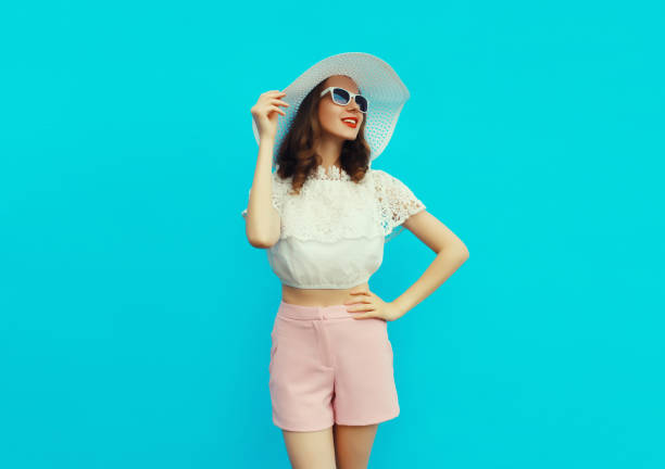 Beautiful caucasian young woman model posing wearing white summer straw hat on blue studio background