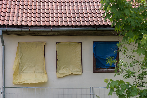 A view of a house under renovation with three windows covered with yellow and blue materials.