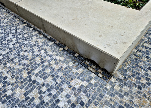 large format paving made of gray granite. the water is drained in the rain through a slotted stainless steel channel which is sunk under the surface of the tile. brickwork, slotted