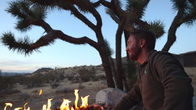 Carefree man relaxing in his backyard at dusk, staring at fire pit, tranquil scene