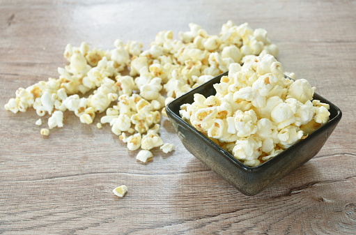 salty popcorn spreading  from bowl on wooden table