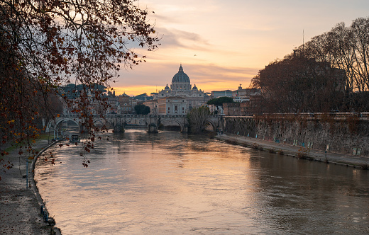 breathtaking beauty of St. Peter's Basilica in Rome, Italy, as the sun sets, casting a warm glow on the majestic structure, while the Tiber River gracefully reflects the colors of the Roman sky
