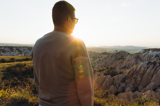 Rear view of a man admiring  bright sunset during the road trip with view of the beautiful rock formations from above in Turkey