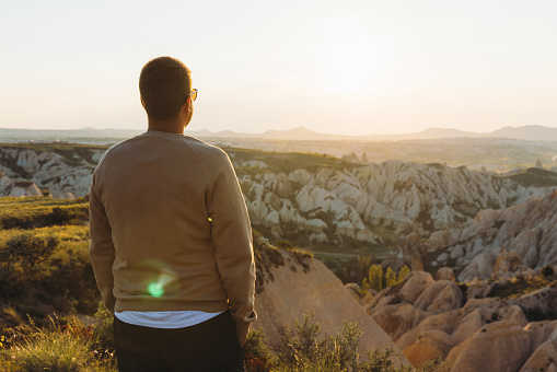 Rear view of a man admiring  bright sunset during the road trip with view of the beautiful rock formations from above in Turkey